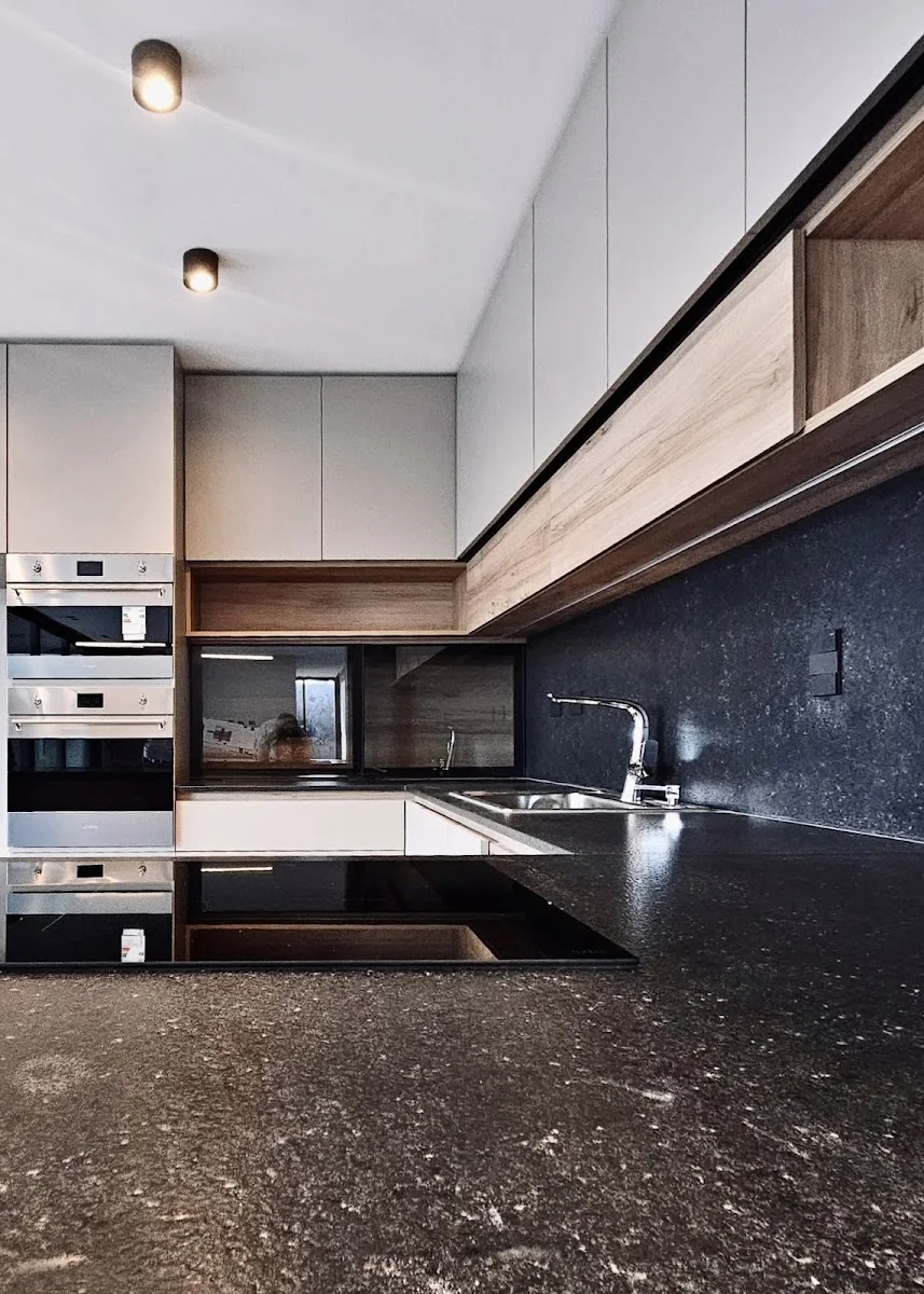 Cocina con cubierta de piedra oscura, muebles de madera y hornos empotrados