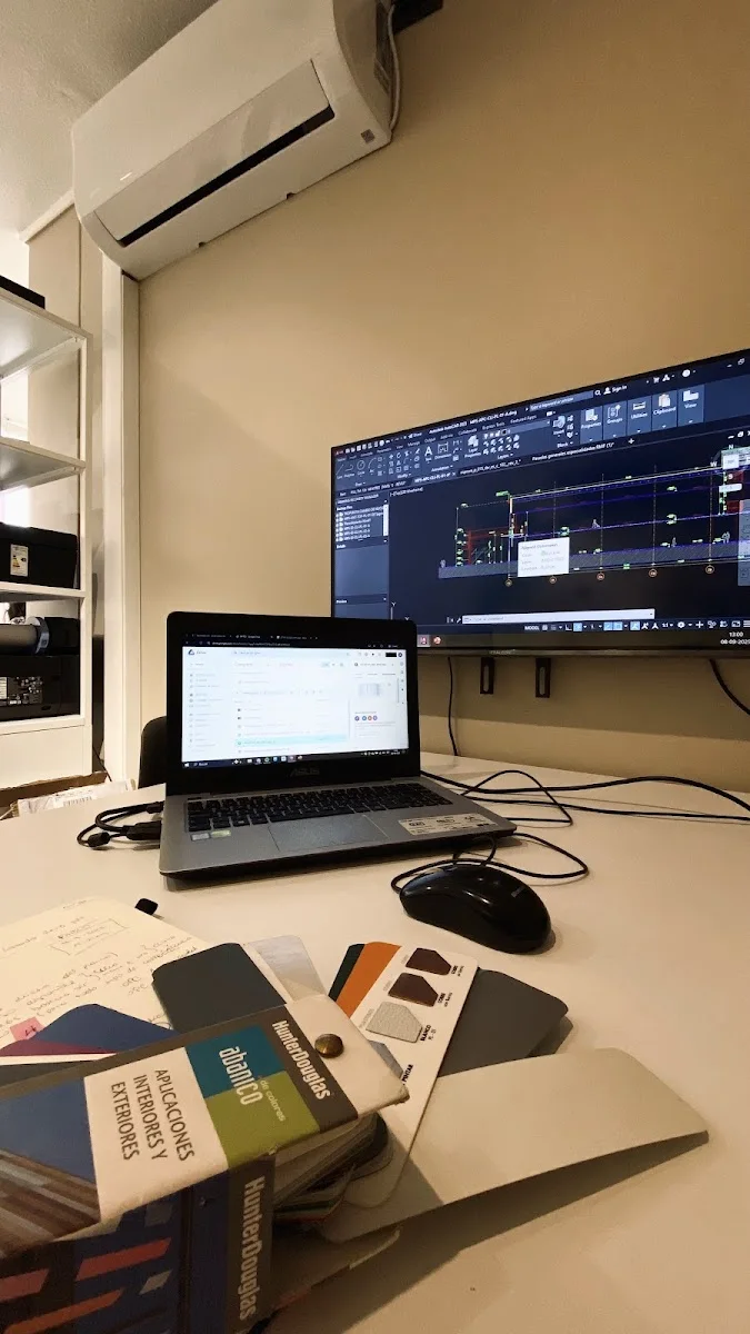 Escritorio del estudio con planos en pantalla y notas de trabajo